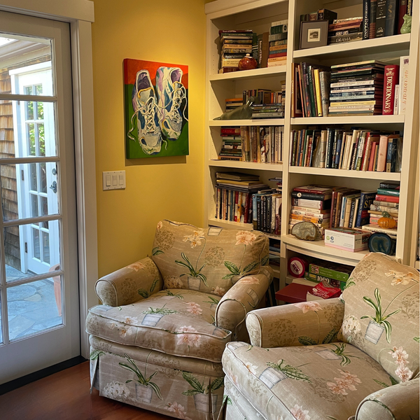 Kearsley Home made an old entry into a mini libary and french door exit out to a court yard in sonoma for a renowned author and her art collector husband. They love color so the walls are a cozy yellow with linen floral upholstered chairs and full white bok shelves and a painting of sneakers.
