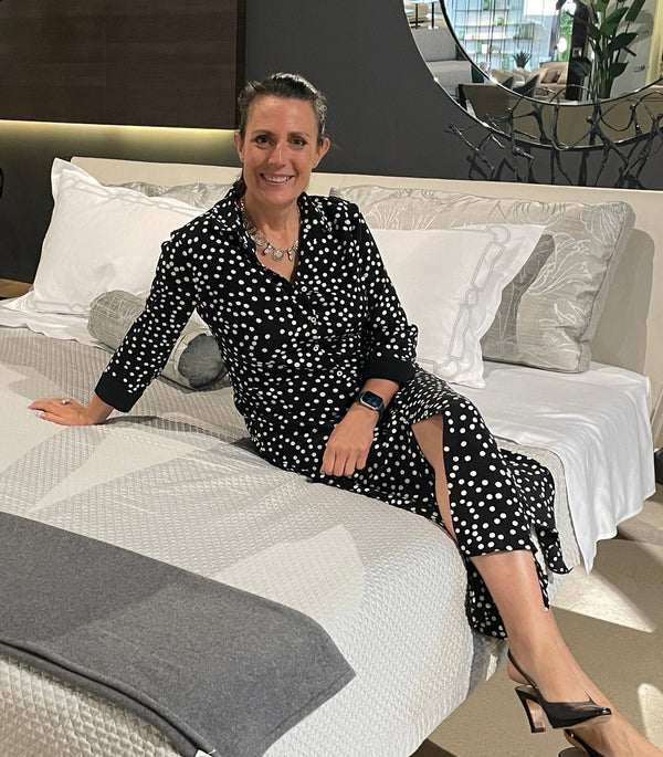 Heather Kearsley Wolf seated on a luxury bed in Dallas before her Understanding and Caring for Fine Linens presentation.