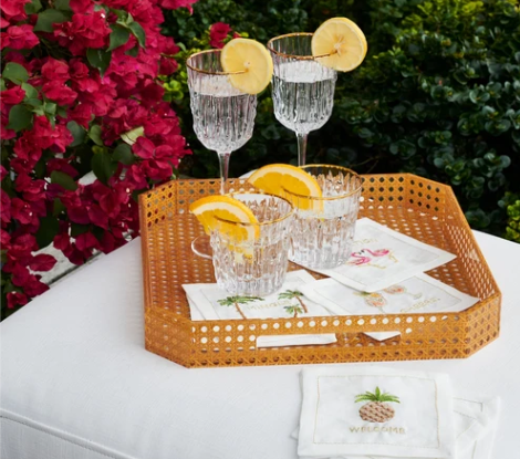 Set of eight white Kim Seybert Mingle cocktail napkins with colorful hand-embroidered celebratory phrases. on a rattan tray with glasses in a garden.  Garden party napkins.  Cocktail party napkins.  