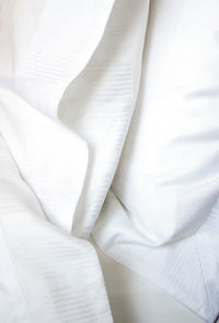 Photo by Kay Bowling of a Soleil Border on a pillowcase, Euro Sham, top sheet, and duvet cover.  Soleil border is an abstracted ray of the sun white on white jacquard weave.  The body of the linens is Soleil 300 thread count sateen.  Part of Kearsley Daily Essentials.